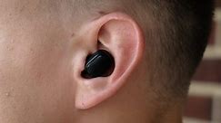 A man inserts a wireless earpiece or hearing aid into his ear, close-up