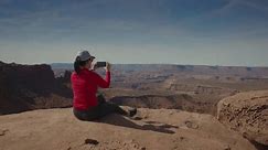 Woman sitting on overlook photographing scenic view at canyonlands national park, utah, united states