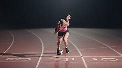 Front view of a female athlete starting her sprint on a running track. Runner taking off from the starting blocks on running track. Zoom camera. Slow motion