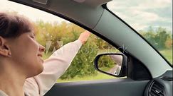 Smiling young travel woman riding car with hand waving window closeup side view. Happy relaxed female enjoy freedom road trip inside automobile with positive emotion. Summer countryside highway