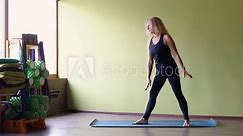 A middle-aged woman practicing yoga, performing the Ardha Chandrasana exercise, crescent pose, training alone in a room on a mat