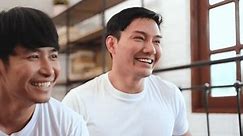 LGBTQ Asian gay couple wearing white t-shirts smiling faces looking happy while watching TV together, gay pride or LGBTQ concept.