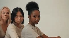 caucasian, asian black american ladies in casual wear sitting one by one, behind each other posing at camera together isolated studio background Ladies of different ethnicity appearance. lesbians