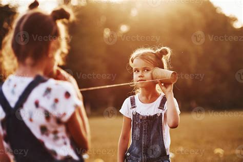 Two female kids stands in the field and talking by using string can ...