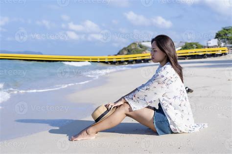 Worried woman sitting on beach with a straw hat on her knees tropical beach by the sea in sunny ...
