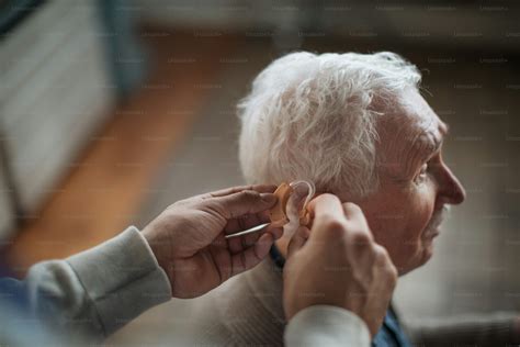 A caregiver helping seniot man to insert hearing aid in his ear. photo ...