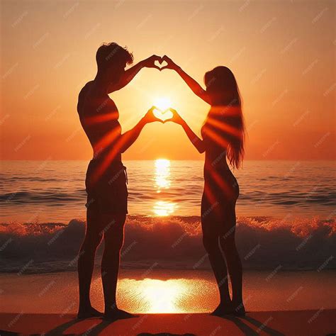 A couple in love making a heart shape with their hands on the beach at ...