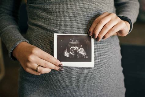 Stylish pregnant woman holding ultrasound scan of her baby on her baby ...