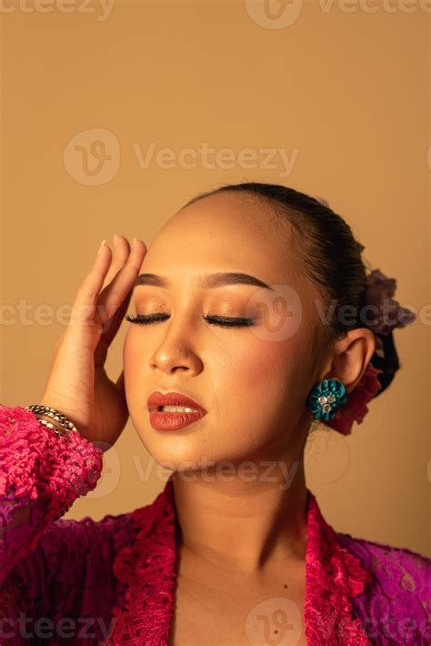 Portrait of Balinese woman with pink dress pose with hands on the face ...