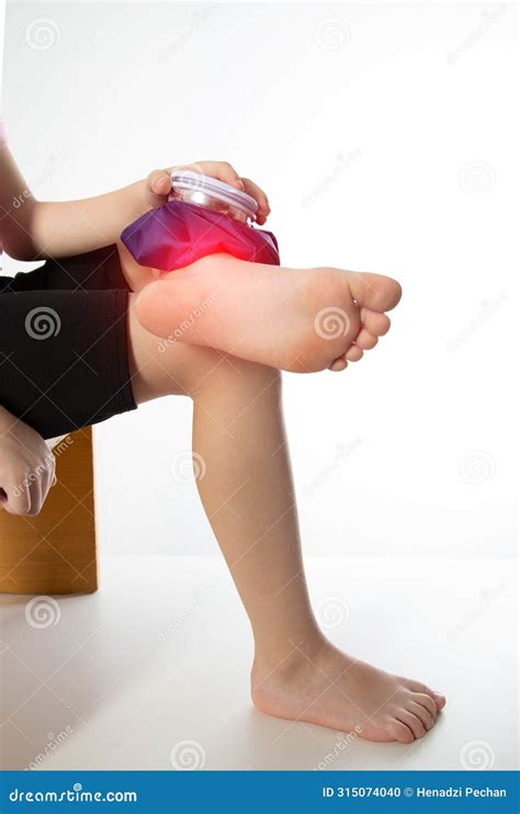 A Girl Applies a Blue Medical Bag with Ice To Her Ankle Joint for a Bruise on Her Leg. Local ...
