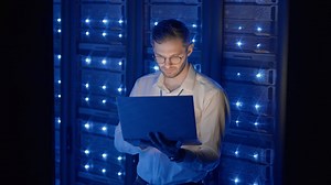 Male network engineer doing a system check standing in the server room with his laptop. At data center men server specialists inspecting working system and hardware of rack server computer cabinets | Premium Stock Video Footage