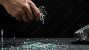Smashing Alarm Clock - A hand forcefully smashes a silver alarm clock, sending shards of glass flying across a dark surface. Stock Video