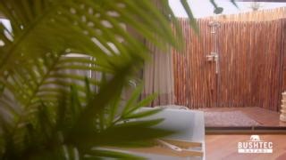 Introducing the Alphecca tent, another new addition to our Bushtec display area. This luxury tent boasts a distinctive style with a captivating tensile roof structure, seamlessly blending modern elegance with traditional safari aesthetics. Its thoughtfully designed interior utilizes shop fitting to divide open space into a wardrobe dress-up area, a cozy bedroom, and a private bathroom. This tent design features an outdoor shower with a roll-up canvas wall, creating a unique bathing experience th