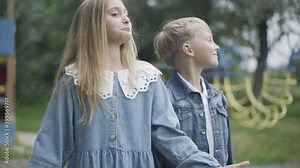 Excited girl talking and gesturing as shy boy kissing her on cheek. Romantic Caucasian children chatting outdoors on cloudy summer day. First love romance and dating concept.