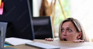 Scared woman peeks out from under table looking at screen