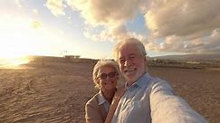 Portrait de deux personnes âgées et matures profitant de l'été à la plage en regardant la caméra prendre un selfie avec le coucher de soleil à l'arrière-plan. Deux personnes âgées actives voyageant à l'extérieur.