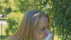 woman smelling flowering plant and sneezing into tissue, illustrating pollen allergy. Woman experiencing allergic reaction outdoors in park.