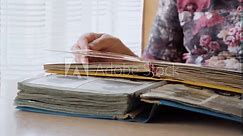 An adult woman leafs through an old photo album with nostalgia. The close-up image shows the hand of an elderly woman with an old photo album, which shows photos of deceased relatives.