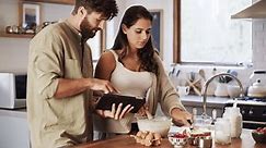 Couple, tablet and cooking in home kitchen for reading, search or video for recipe with helping hand. Woman, man and happy with info, checklist and website for diet, nutrition or wellness in house