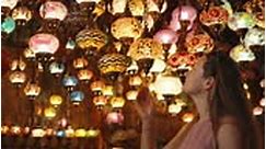 A young woman is examining antique colorful Turkish lamps hanging...
