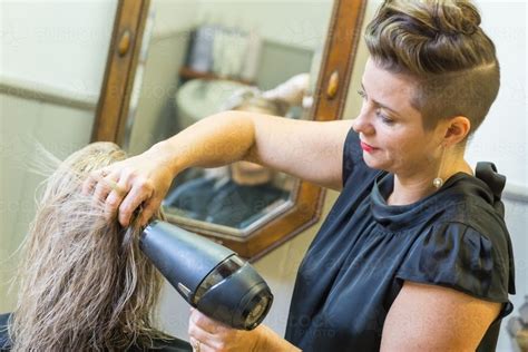 She recommends drying your hair using a small microfiber towel, which not only reduces tension but also decreases friction. A hairdresser blow drying a ladies hair in a salon ...