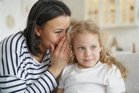 Mother or babysitter whispering sharing secret with kid daughter